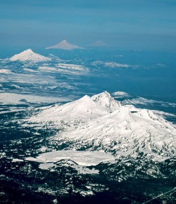 An aerial view of the Cascade volcanic peaks in Oregon, with the Three Sisters in the foreground, and Mts. Washington, Jefferson, Hood, and Adams extending northward