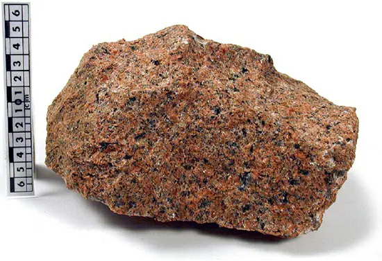 A sample of granite from Victoria, Australia, featuring prominent alkali and plagioclase feldspar minerals (in pinkish-red and gray colors, respectively), along with quartz (shiny) and black mica.