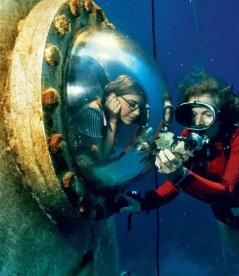 Marine biologist and explorer Sylvia Earle, wearing SCUBA gear, examining a damaged coral reef sample.