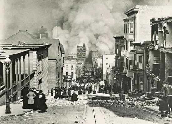 A photograph capturing the view down Sacramento Street, showing the wreckage and subsequent fire resulting from the San Francisco earthquake on April 18, 1906.