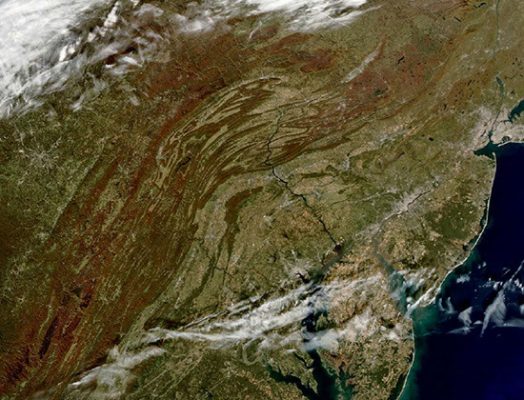 This satellite image shows the ancient, folded, and eroded remnants of the Appalachian Mountains, depicted as brown bands, in the northeastern United States. New York City is visible just above the center right of the image.